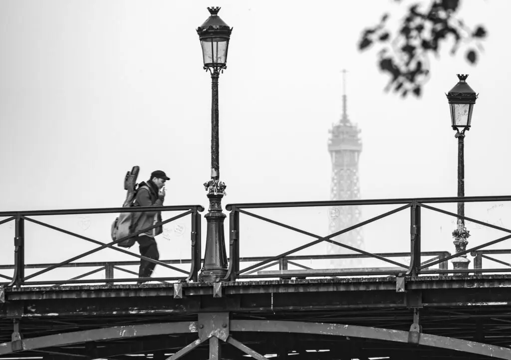 Musicien traverse un pont de Paris avec la Tour Eifell derrière 