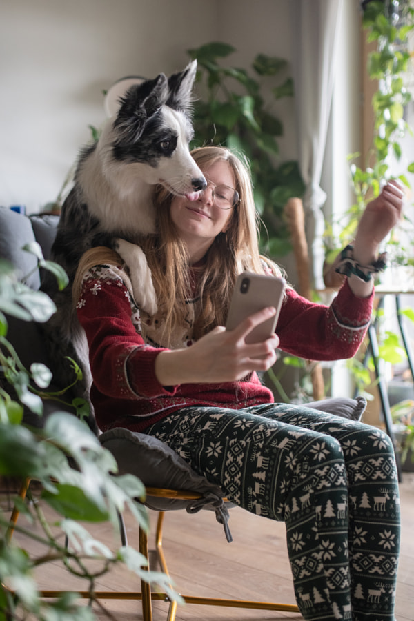 Femme souriante prenant selfie drôle par téléphone portable tout en étant assis sur une chaise avec un chien à la maison par Iza ?yso?  sur 500px.com